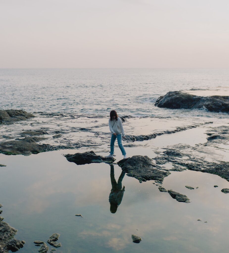 person-stands-on-rocks-poking-out-of-the-ocean-shoreline